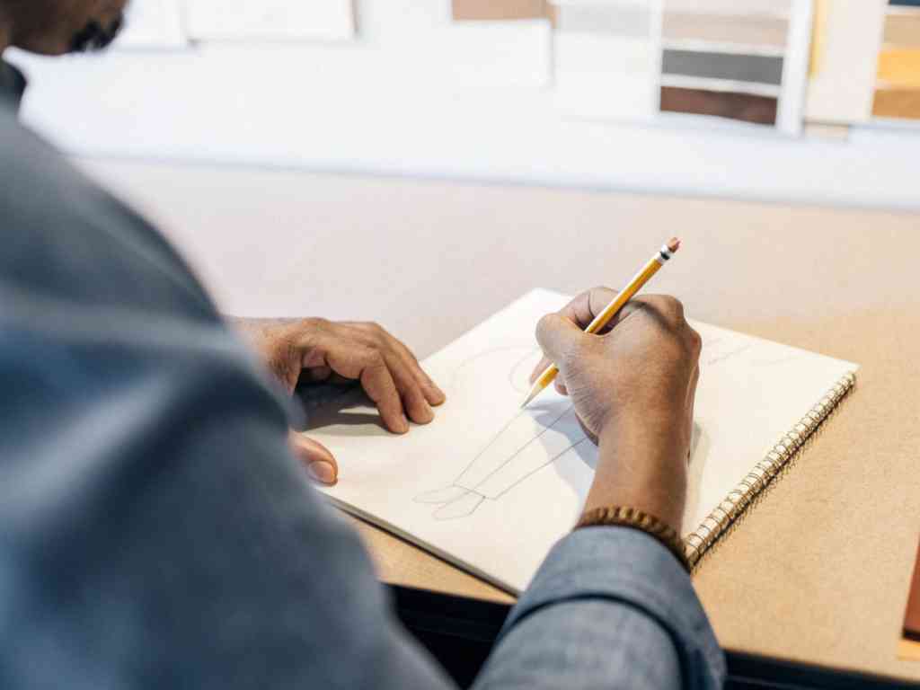 Person sketching fashion design in notebook with pencil.