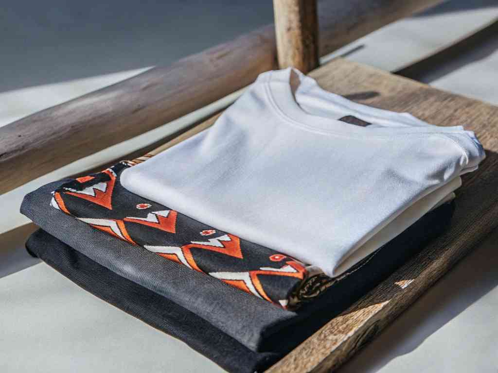 Folded T-shirts in neutral and tribal prints on wood.