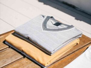 Stack of folded gray and mustard V-neck t-shirts on wooden bench.