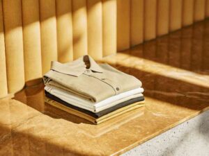 Folded polo shirts in beige, white, and mustard on stone surface