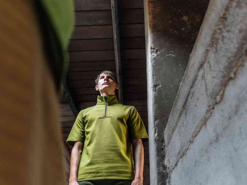 Man in green quarter-zip standing under industrial ceiling light.