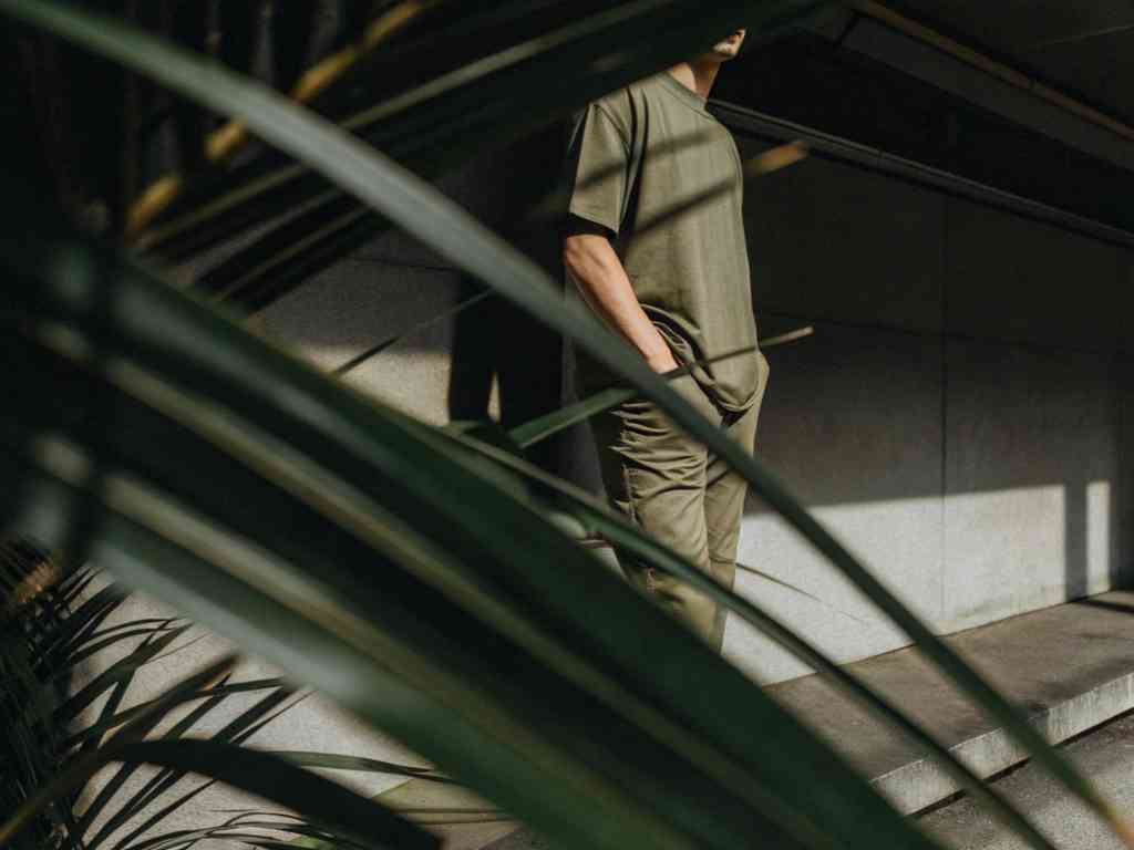Man in olive green outfit standing behind tropical leaves