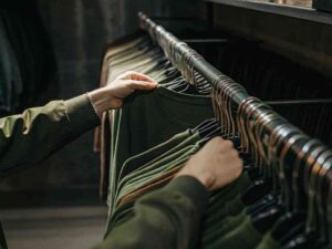 Person browsing green t-shirts on clothing rack