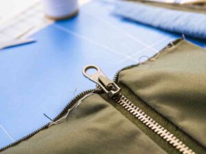 Close-up of green zipper sewn on olive fabric on blue cutting mat