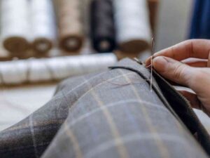 Tailor hand-sewing plaid fabric with brown thread