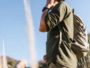 Hiker in olive green shirt and backpack under clear sky.