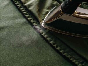 Steam iron pressing green fabric on ironing board.