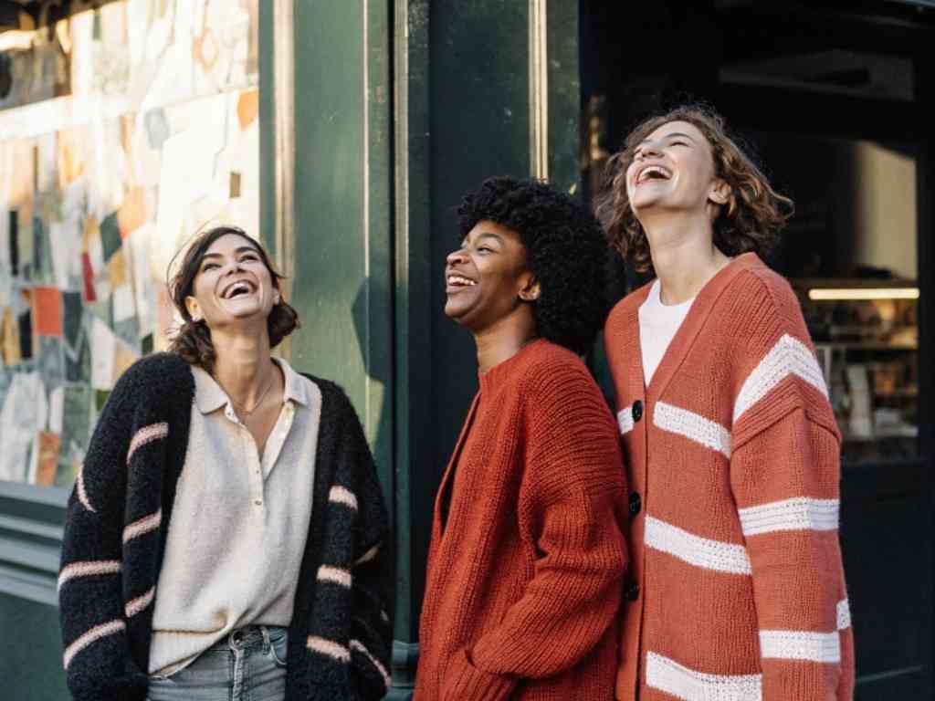 Three women laughing in cozy cardigans outdoors