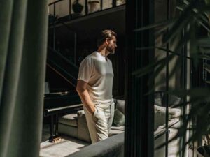Man in white satin-like t-shirt standing in modern living room.