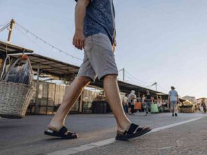 Man in light shorts and sandals walking through an open-air street market.