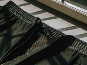Close-up of black athletic shorts featuring mesh lining and elastic waistband under natural sunlight.