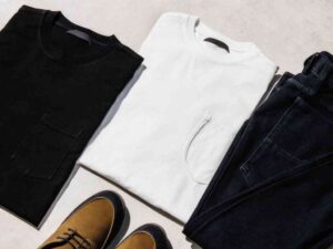 Folded black and white shirts, jeans, and brown shoes on light background.