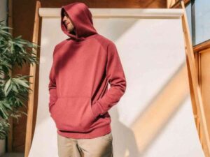 Man in red hoodie posing casually in sunlit indoor studio.