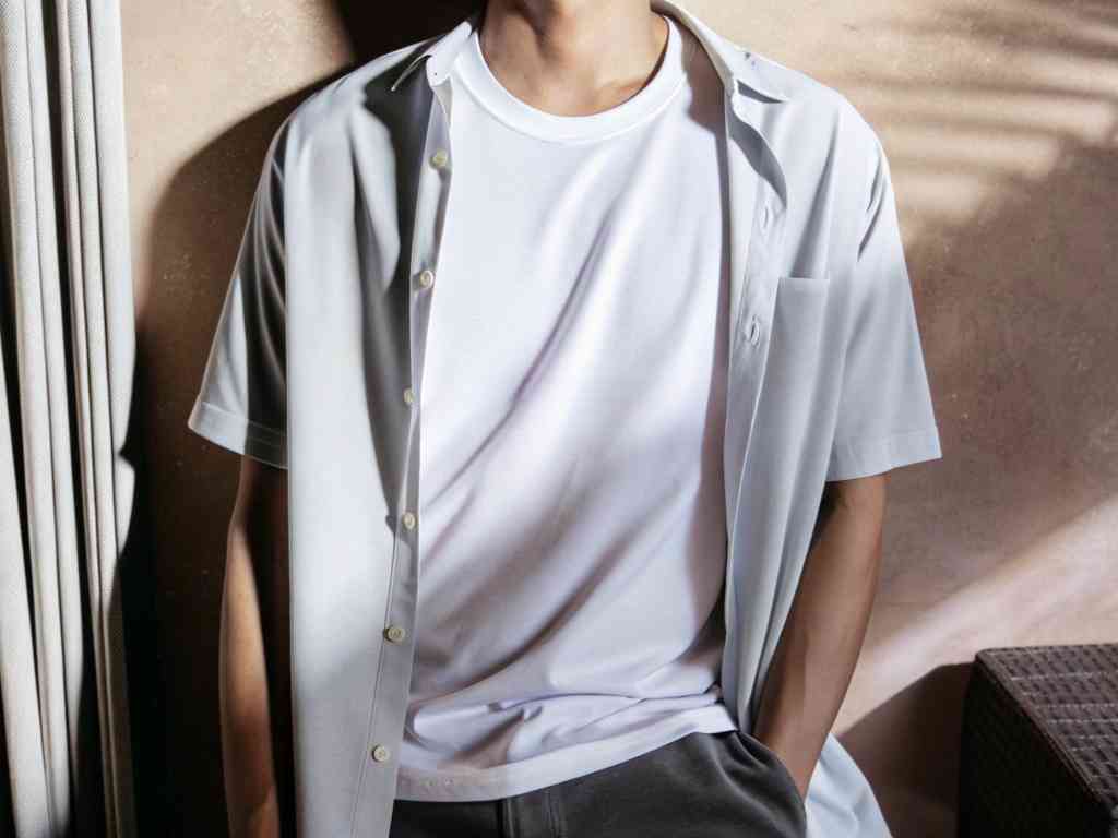 Man in white shirt and open short-sleeve overshirt, relaxed pose.
