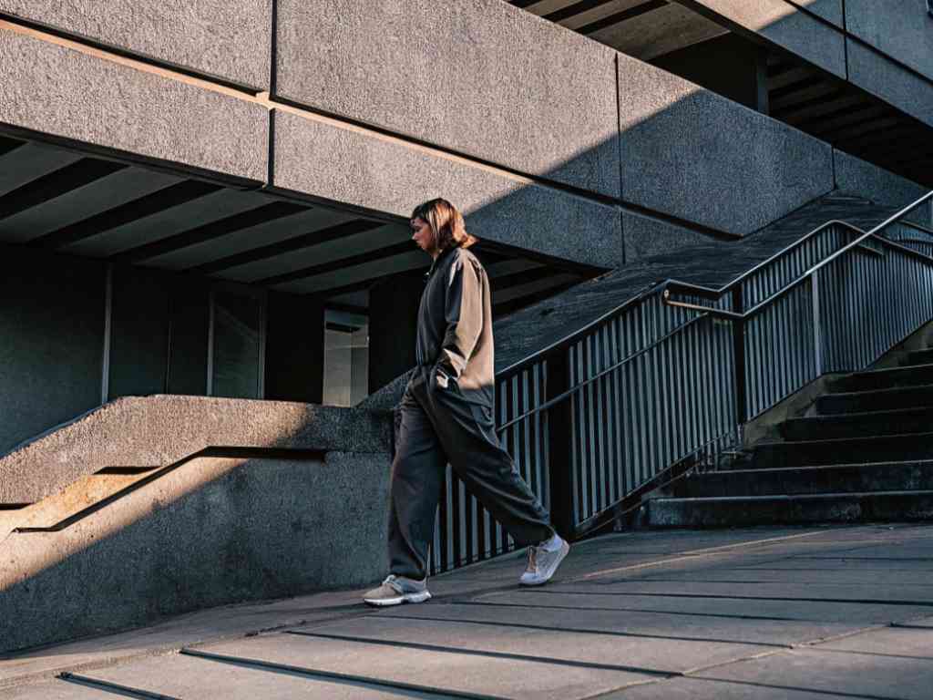 Woman in oversized dark outfit walking past concrete building