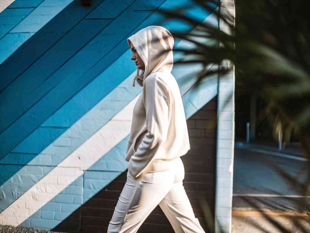 Woman in cream hoodie walking by blue mural
