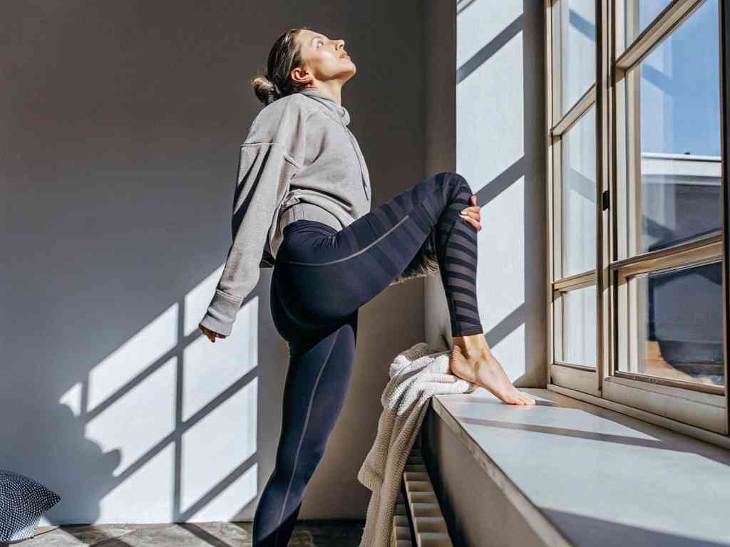 Woman stretching indoors wearing black striped leggings
