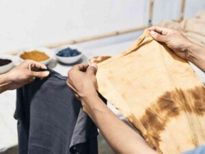 People comparing tie-dye and dark T-shirts by dye bowls.