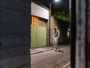 Man in hoodie and vest standing alone on quiet street at night