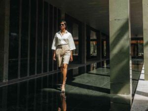 Woman in white blouse and beige shorts walking confidently