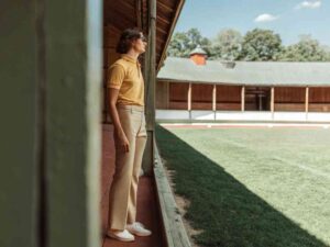 Man in retro yellow polo shirt and beige trousers standing beside a grassy sports field