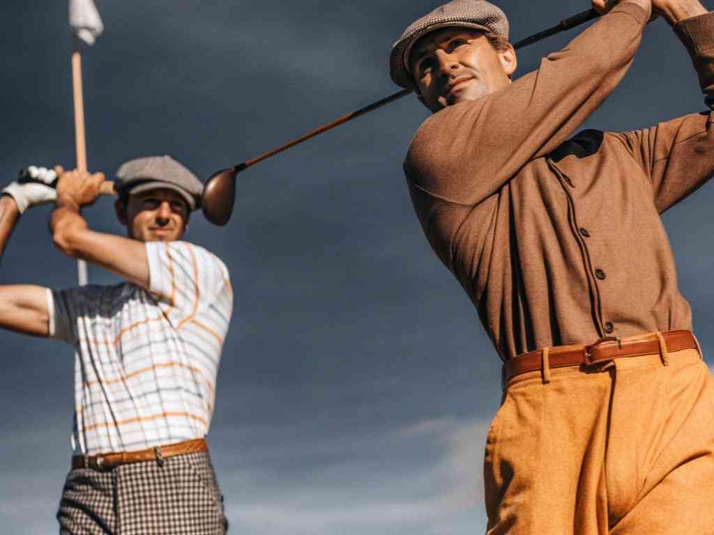 Two men in vintage golf outfits mid-swing