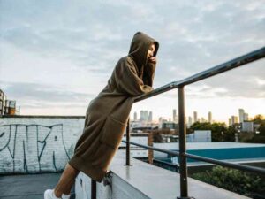 Woman in oversized hoodie leaning on rooftop railing at sunset