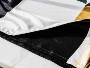 Satin fabric with color-blocked pattern in black, white, and gold.