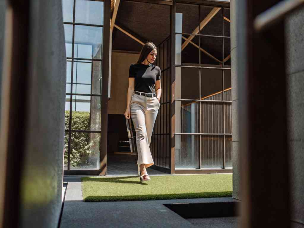 Woman in black top and beige pants outside modern building.