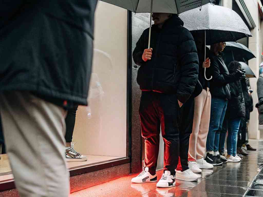 People in streetwear and sneakers queuing in rain with umbrellas