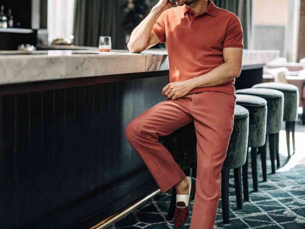 Man in rust-colored polo and trousers sitting at upscale bar