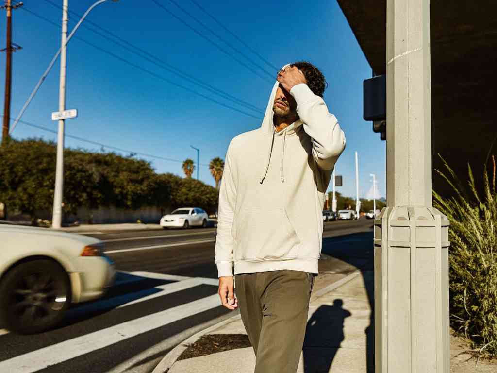 Man in cream hoodie walking on sunny street