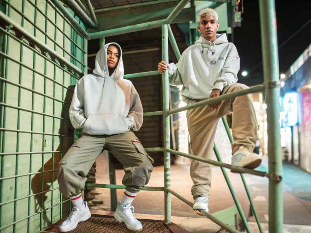 Two people in hoodies posing in urban night setting.