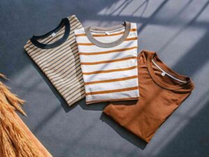 Three folded striped and solid color t-shirts on dark surface.