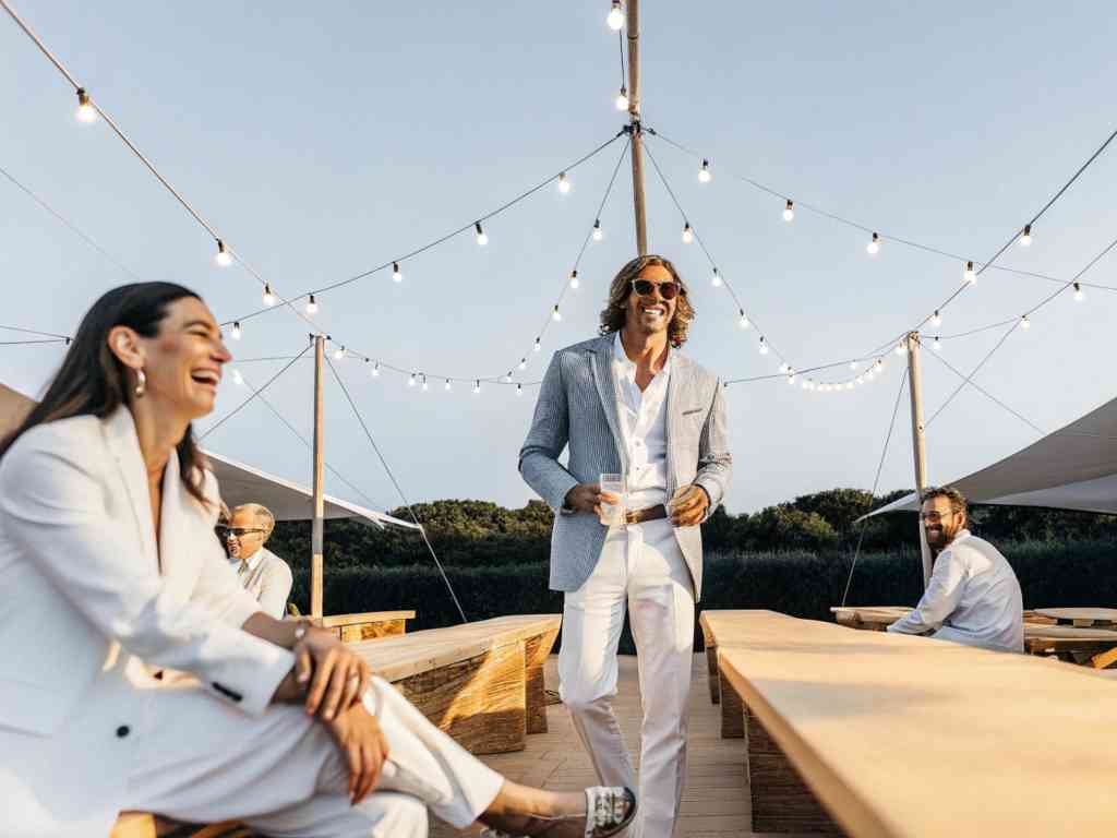 Guests in stylish suits enjoying a sunny outdoor gathering event.