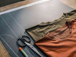 Flat lay of folded t-shirts with tailoring tools and chalk.