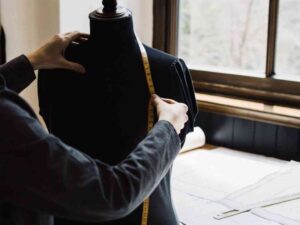 Designer measuring black dress form with yellow tape measure.