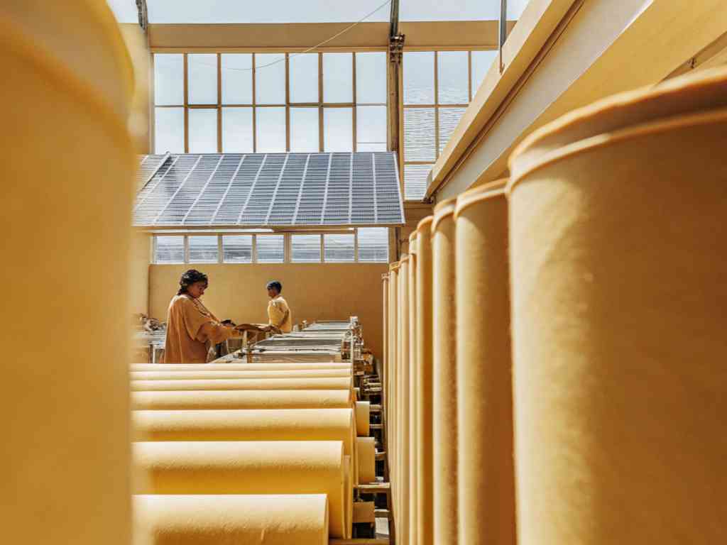Workers processing yellow fabric rolls in a sunlit textile factory.