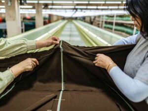 Textile workers checking brown fabric with green zipper