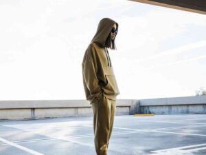 Model in tan hoodie and joggers standing in rooftop lot