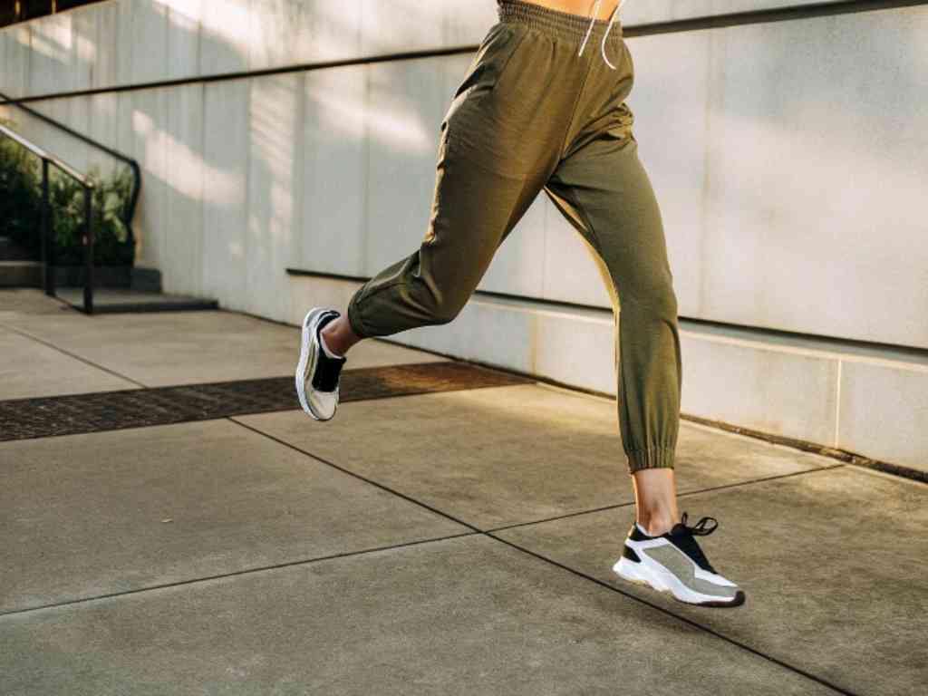 Woman running in olive slim-fit joggers and black-white sneakers