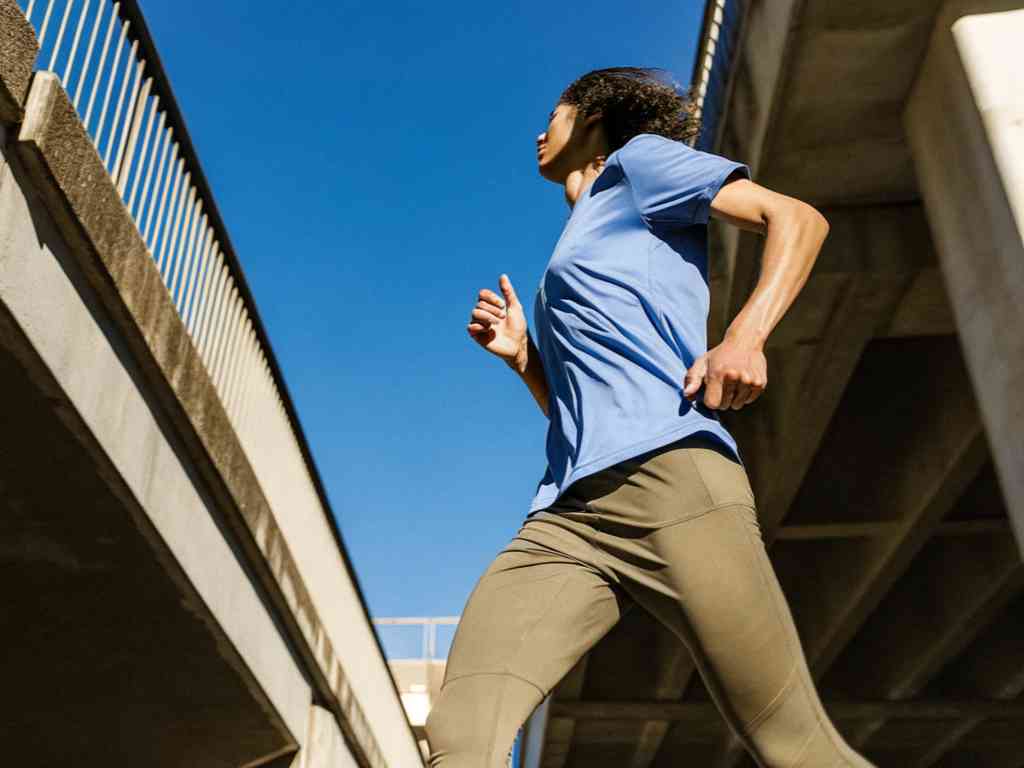 Woman jogging in blue top and leggings under city overpass.