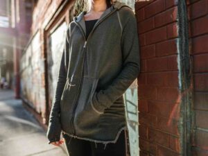 Woman in dark zip-up hoodie leaning against brick wall