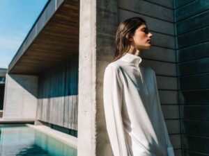 Woman in white high-neck top near modern building.