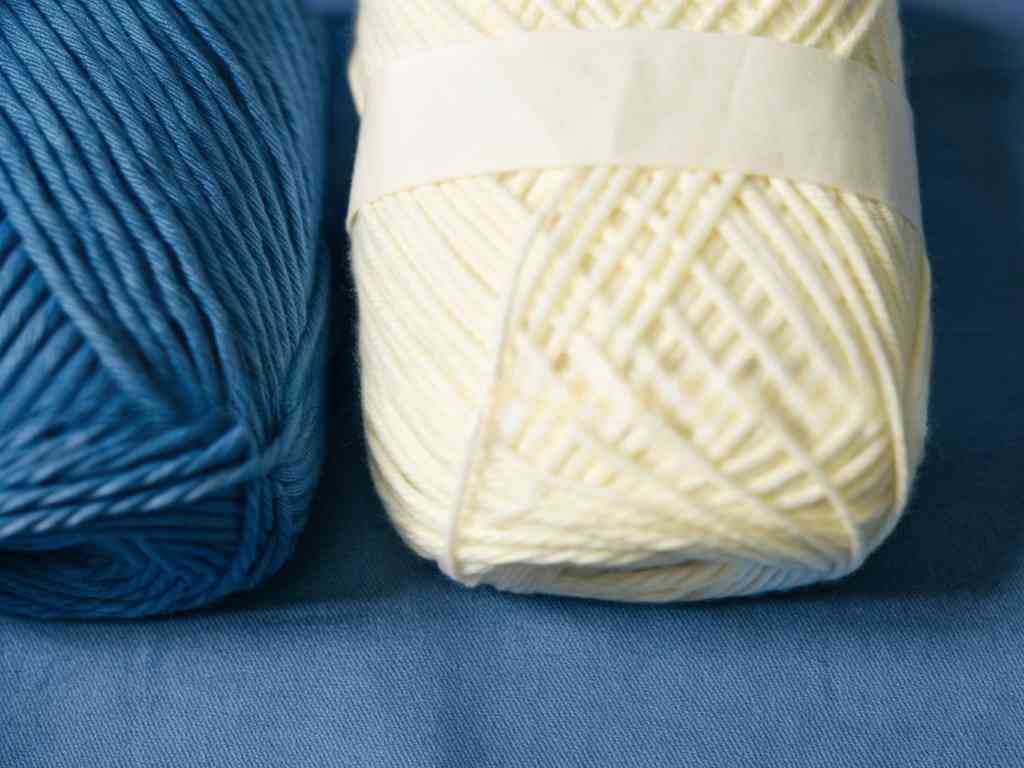 Blue and cream yarn balls on blue fabric background.