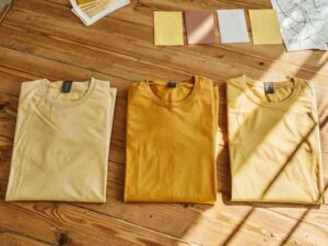 Three folded yellow t-shirts on wooden table with color swatches