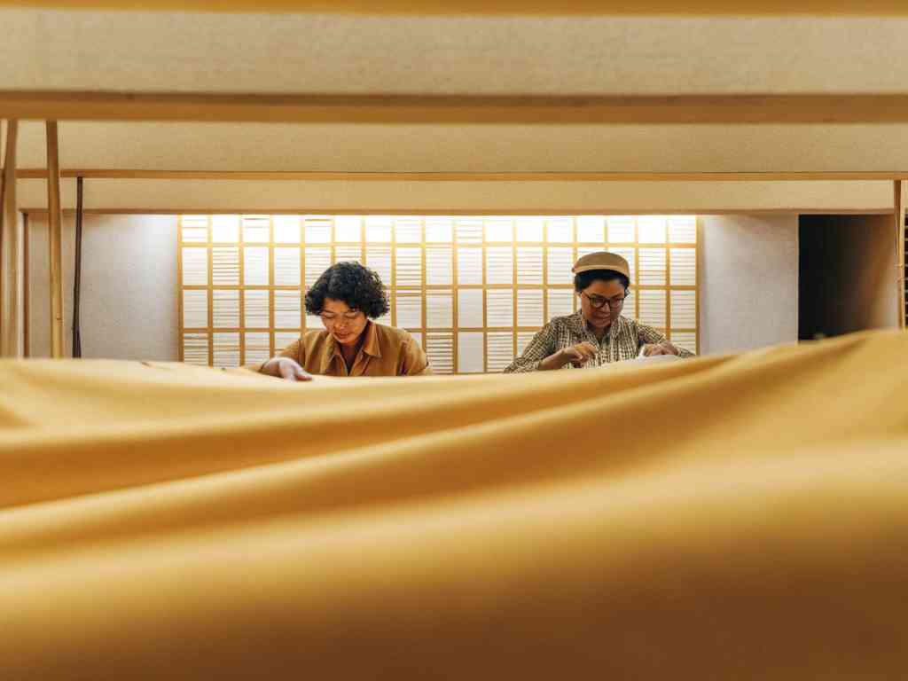 Two women working with yellow fabric in warm-lit studio