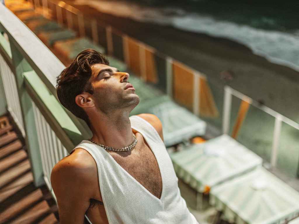 Man in white knit v-neck tank top on balcony.