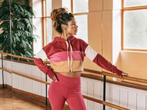 Fitness model in colorblock cropped hoodie and leggings stretching in studio.
