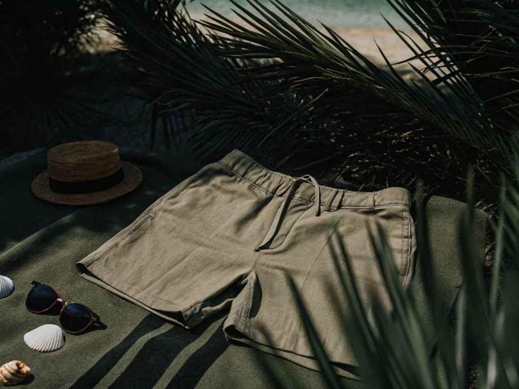Olive green beach shorts with sunglasses and straw hat by the shore